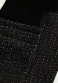 Sorte sokker med et struktureret mønster og små grå prikker. Materialet ser ud til at være strikket med en let glans, der fremhæver det geometriske design.