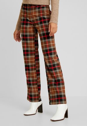 Braune karierten Hosen mit roten, schwarzen und cremefarbenen Mustern; Design mit weitem Bein; der Stoff wirkt weich. Kombiniert mit weißen Stiefeln mit Absatz.