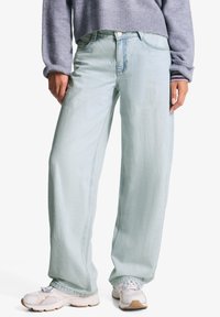 Svijetloplavi široki traperice od denima, s dugmetom zatvaranjem, prednjim džepovima i suptilnom teksturom, uparenih s bijelim tenisicama.