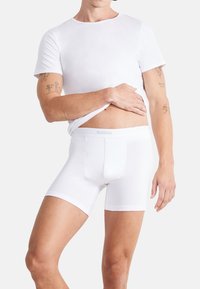 Białe bokserki Sloggi z miękkiego materiału, elastycznym paskiem w talii i dopasowanym krojem. Model nosi dopasowaną białą koszulkę.