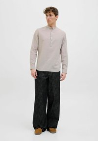 Langærmet, lys beige henley-skjorte med tre knapper, parret med løstsiddende, mørke strukturerede bukser og brune slip-on sko.
