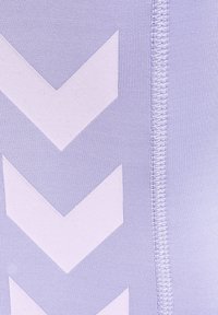 Zbliżenie na lawendową tkaninę z trzema białymi strzałkami w kształcie chevron skierowanymi w dół obok pionowego szwu.