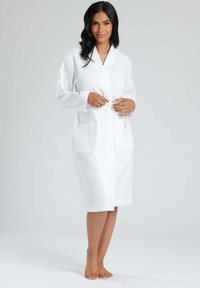 Accappatoio bianco in maglia waffle con maniche lunghe, cintura in vita e tasche frontali, caratterizzato da un motivo testurizzato e design fino al ginocchio.