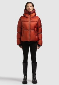 Puchowa czerwona kurtka z wysokim kołnierzem, zamkiem z przodu i dwoma bocznymi kieszeniami. Całość dopełniają czarne spodnie i czarne kozaki za kolano.