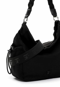 Zwarte stoffen tas met een gevlochten bovenhandvat, verstelbare schouderband met een logo-patroon en een zijvak met rits. Zachte textuur, modern ontwerp.