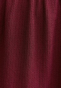 Czerwony, teksturowany materiał z pionowym prążkowaniem i subtelnym połyskiem, prezentujący bogaty, głęboki kolor i złożony wzór.