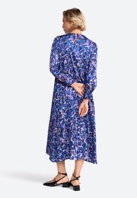 Langärmliges A-Linien-Kleid aus einem lebhaften blauen Stoff mit abstrakten Blumenmustern in Pink und Lila. Verfügt über einen Rückenschlitz und einen knöchellangen Saum.