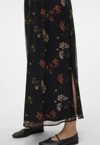 Černá květinová maxi sukně s průsvitnou texturou, zdobená červenými a krémovými květinovými vzory, s bočním rozparkem, kombinovaná s černými balerínami.