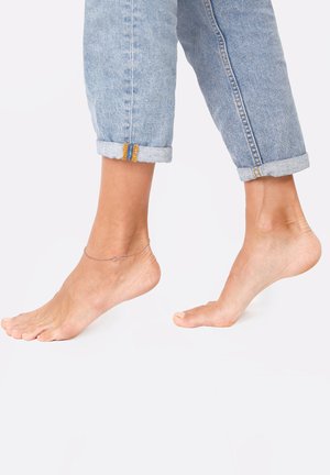 Ankelkæde med et uendelighedssymbol designet på en bar ankel, parret med opkørte lyseblå denimjeans. Glat hudtekstur synlig.