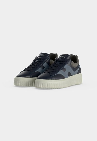 Paire de baskets bleu marine et grises à lacets avec semelles blanches épaisses rainurées sur fond uni.