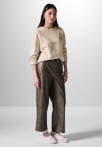 Sudadera beige con puños acanalados, combinada con pantalones de piel sintética verde oliva oscuro de cintura alta que presentan costuras frontales. Zapatillas rosas completan el conjunto.