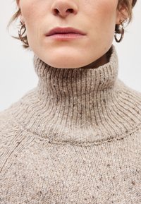 Beige pletený rolák s jemně rytou strukturou a tečkovanými detaily, navržený tak, aby těsně obepínal krk.