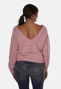 Maglione rosa lavorato a maglia con scollatura a V profonda sul retro. Presenta tre fiocchi decorativi lungo la spina dorsale. Il materiale appare morbido con una leggera lucentezza.