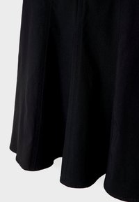 Sort stof nederdel kant med synlige lodrette sømme, glat tekstur og let udvidelse mod en lys grå baggrund.