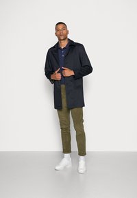 Navy trench coat with a classic collar, button closure, and long sleeves, paired with olive corduroy pants and white sneakers.