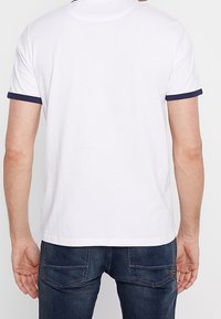 Vit kortärmad polo med marinblå detaljer på ärmar och krage. Mjukt bomullsmaterial, ren design, bakvy visad.