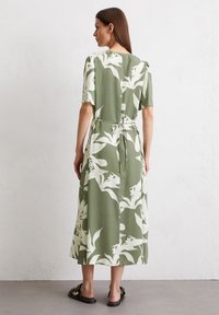 Lungo vestito verde con motivo floreale bianco, maniche corte, cintura annodata in vita e lunghezza midi fluida. Indossato con sandali flats.