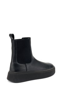 Botín de cuero negro hasta el tobillo con paneles laterales elásticos, suela de goma acanalada y una pequeña lengüeta en el talón. Textura suave en todo el botín.