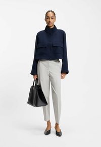 Marineblauw cropped jack met twee voorzakken, gecombineerd met lichtgrijze taps toelopende broek. Zwarte handtas en zwart puntig platte schoenen maken de look compleet.