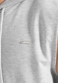 Felpa gilet grigia realizzata in morbido cotone misto. Presenta una piccola placca logo argentata sul petto. Tessuto liscio con cuciture minime.