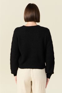 Pull en tricot noir avec une texture côtelée, épaules basses et manches à motifs. Encolure ronde et coupe courte.