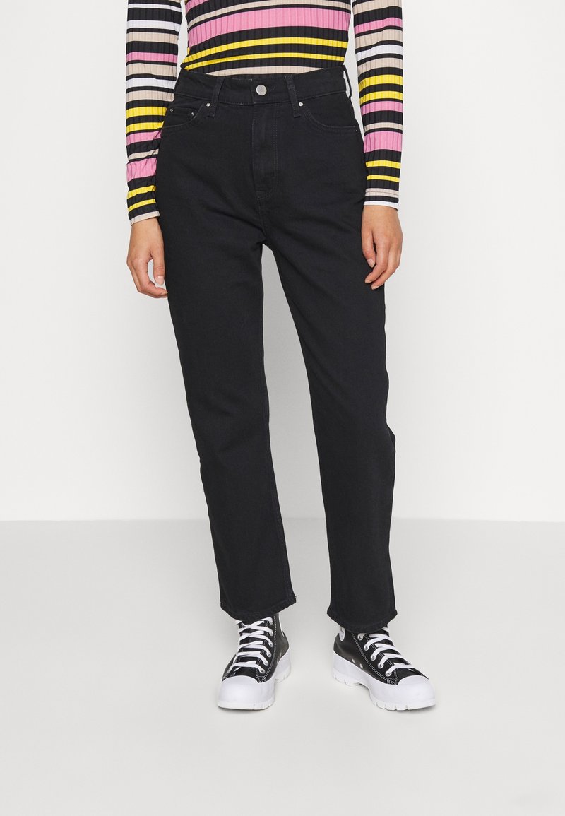 Jean noir taille haute à coupe droite, associé à un haut à manches longues rayé multicolore et des baskets montantes noires.