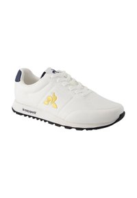 Scarpa sportiva bianca con una texture liscia, caratterizzata da accenti blu navy, logo dorato e suola grigio chiaro; design classico con chiusura a lacci.