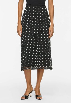 Gonna midi nera con pois bianchi, indossata con sandali neri con tacco aperto e top nero.