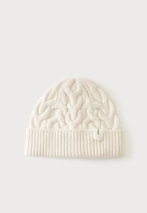 Bonnet blanc tricoté avec motif torsadé et bord-côte replié sur un fond clair uni.