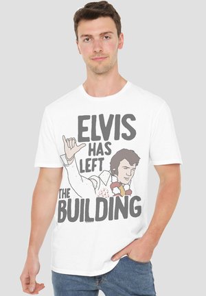 Man wearing white T-shirt with graphic and text "Elvis has left the building" featuring Elvis Presley illustration.