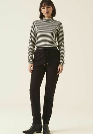 Pantalons noirs ajustés avec taille à cordon de serrage et poches latérales, associés à un haut col roulé à rayures noir et blanc. Tissu texturé.