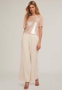 Pailletten blush top met korte mouwen, gecombineerd met wijde crèmekleurige broeken. Open teen strappy heels met een patroon.