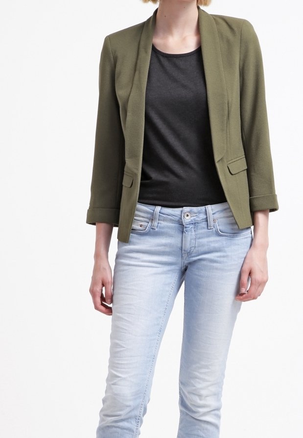 Olivově zelený blazer s šálovým límcem, dvěma předními kapsami a ohrnutými rukávy, kombinovaný s černým topem a světle modrými džíny.