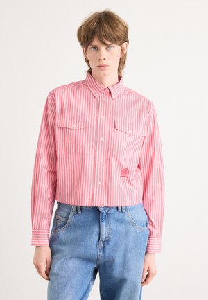 Striped button-up shirt in pink and white, features a collar, two chest pockets, and a cropped design. Worn with blue denim jeans.