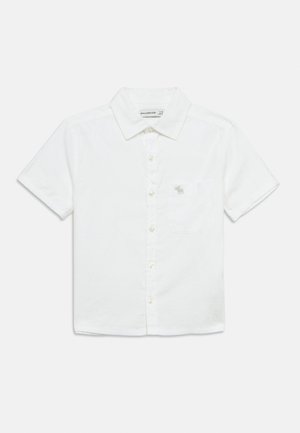 Biela košeľa s krátkym rukávom so zapínaním na gombíky, vyrobená z ľahkej látky. Má ľavú náprsnú kapsu s malým vyšívaným logom.