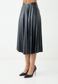 Gonna midi plissettata nera in faux pelle con vita aderente, caratterizzata da molteplici pieghe verticali e una trama liscia e lucida. Abbinata a tacchi neri.