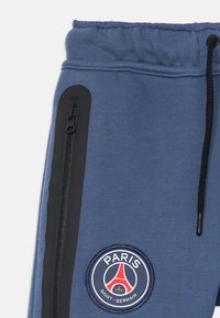 Blaue Sporthose mit elastischem Bund, schwarzem Reißverschlussfach, Kordelzug und Logo-Patch des Fußballvereins Paris Saint-Germain.