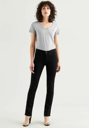 Grijze v-hals t-shirt met een klein rood logo, gecombineerd met zwarte slim-fit jeans en doorzichtige sandalen met hakken. Slank ontwerp, gladde texturen.