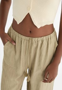 Top court en tricot crème avec fermeture à bouton et ourlet festonné ; pantalon texture léger beige avec taille élastique et cordon de serrage.