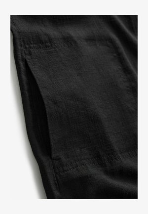 Black fabric close-up showing a textured, woven surface with a subtle sheen. Features a neatly stitched seam and a side pocket opening.
