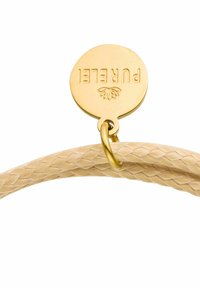 Geflochtenes beiges Lederarmband mit einem goldenen Metallschild, das das eingravierte Wort "PUREL" und ein Blattdesign zeigt.