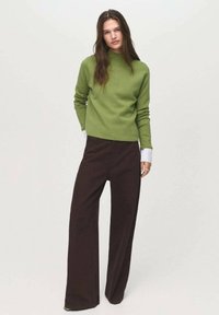 Pull en tricot vert avec col haut, associé à un pantalon ample marron foncé. Le pull a des manches longues et une silhouette courte.