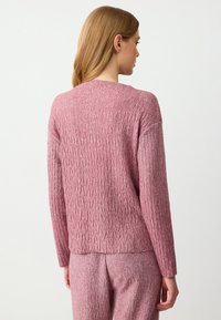 Maglione rosa lavorato a maglia con un motivo a zigzag testurizzato, maniche lunghe e una vestibilità comoda. Il materiale sembra morbido e accogliente.