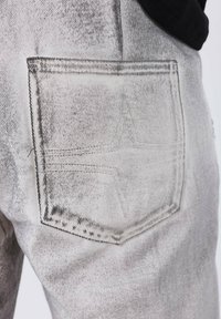 Jeans in denim grigio con una tasca posteriore caratterizzata da un motivo di cucitura visibile e una texture sfumata. Il tessuto presenta un effetto invecchiato.