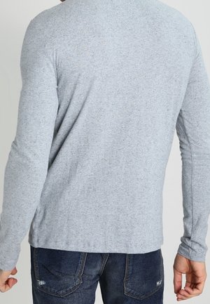 Grå T-shirt med lange ærmer i et blødt, tekstureret stof. Den har rund hals og en figursyet pasform, båret med mørke denimjeans.