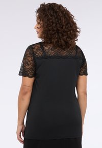 T-shirt nera con maniche corte e sovrapposizione di pizzo. Il retro è completamente nero con una texture liscia, progettato per un fit casual.