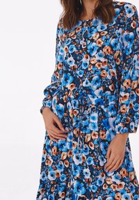 Abito floreale blu con maniche lunghe, vita elastica e orlo arricciato. Presenta un mix di fiori blu, arancioni e beige su uno sfondo scuro.