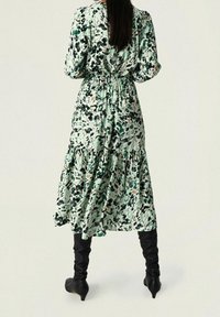 Vestido midi floral en verde menta con patrones en negro y crema, con cintura ajustada, mangas hasta el codo y falda en capas. Botas negras hasta el muslo.