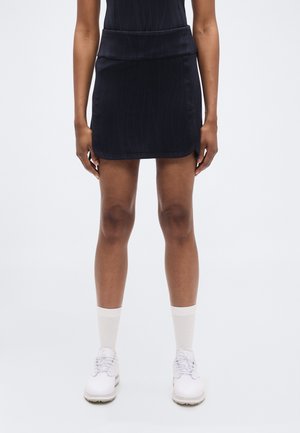 Φούστα σε ναυτικό μπλε με εφαρμοστή μέση, λεία υφή και διακριτικά κάθετα σχέδια. Φοριέται με λευκά παπούτσια και κάλτσες για αθλητική αντίθεση.