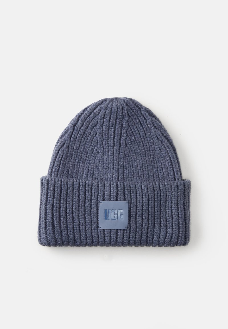 Bonnet en tricot bleu foncé avec texture côtelée, arborant une étiquette carrée UGG à l'avant et un design à revers.